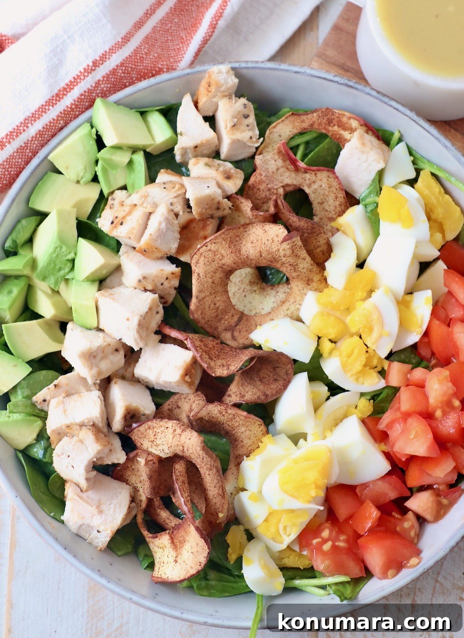 cobb salad in bowl topped with apple chips, eggs, tomatoes, chicken and avocado