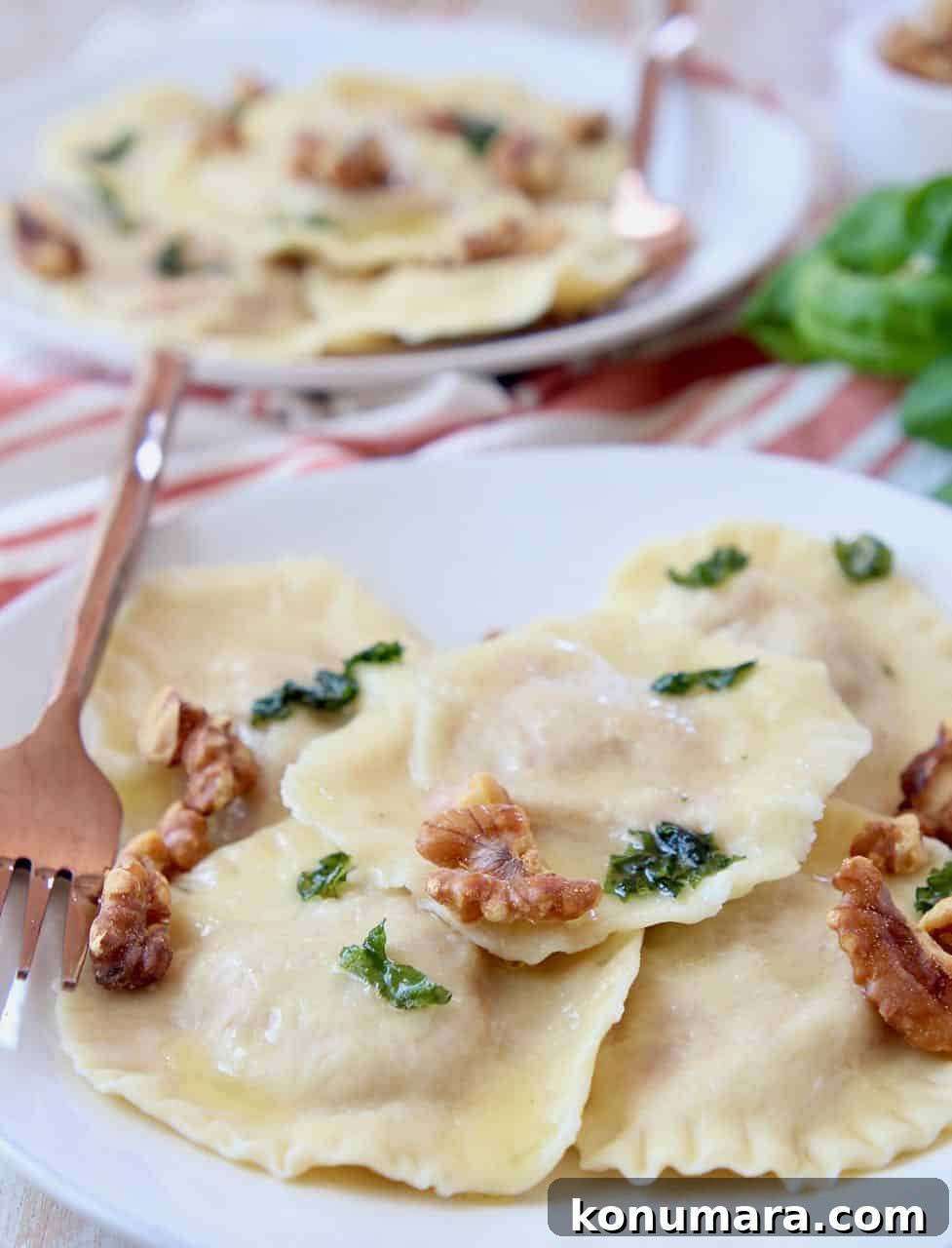 Raviolis on plate topped with basil brown butter sauce and toasted walnuts
