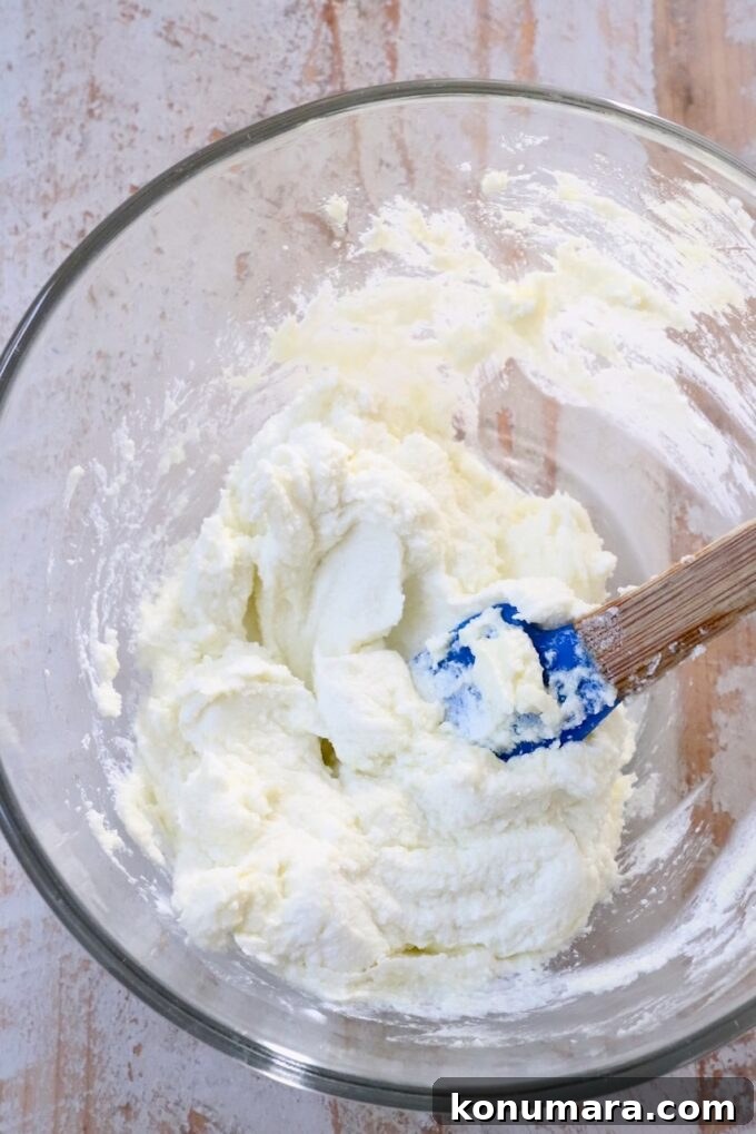 goat cheese whipped in a glass bowl with a blue spatula