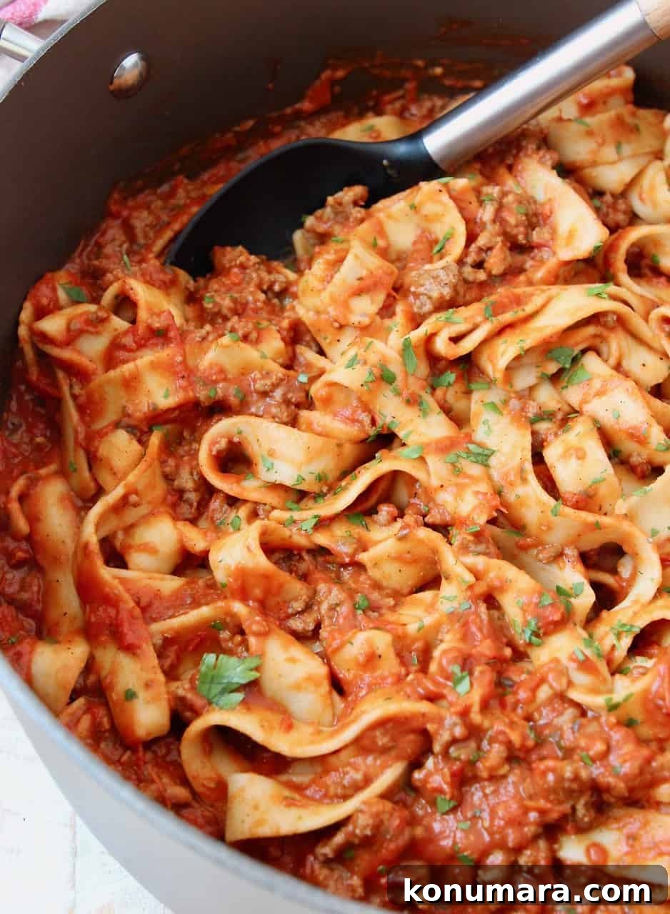 Pasta tossed in meat sauce in large pot with serving spoon in the pot