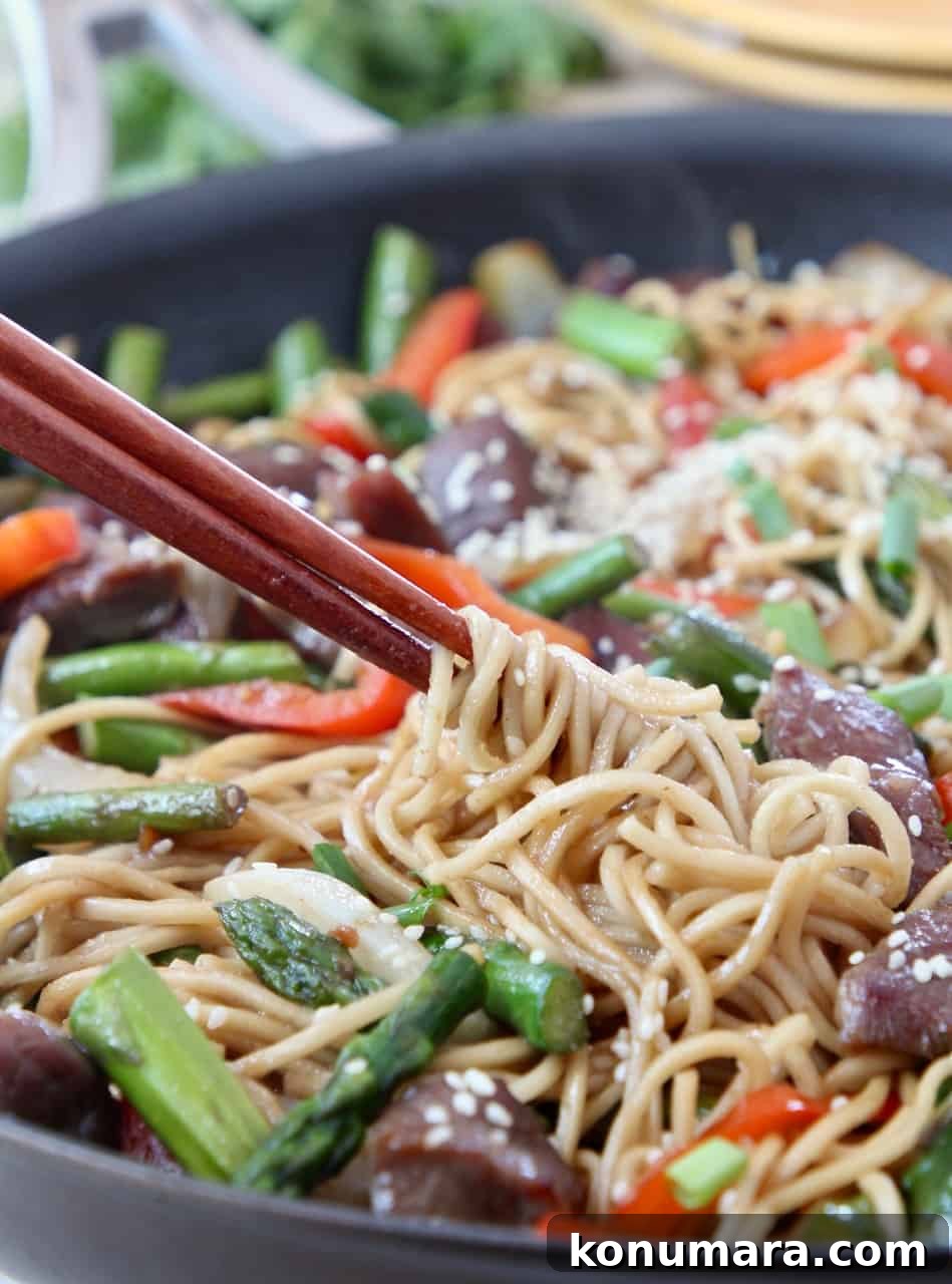 chopsticks swirling noodles in skillet of stir fry
