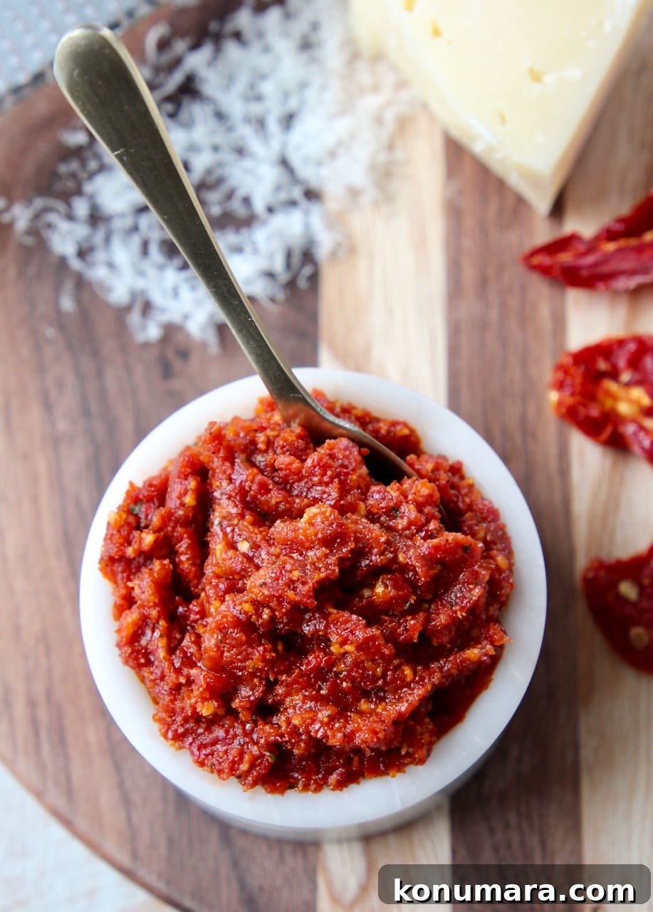 Sun dried tomato pesto in small white bowl with gold spoon in bowl and sun dried tomatoes on the side