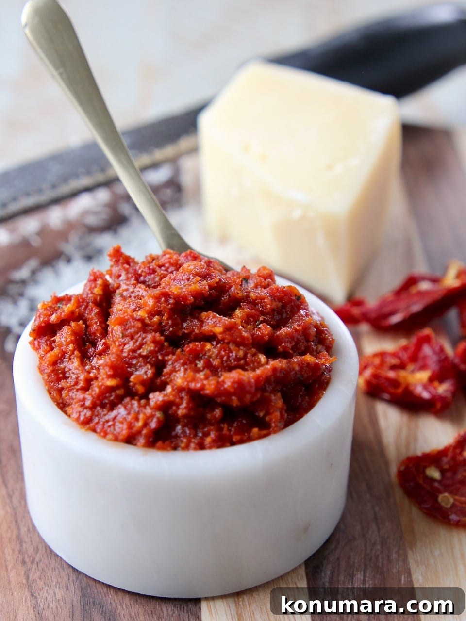 Sun dried tomato pesto in white bowl with parmesan cheese block in background