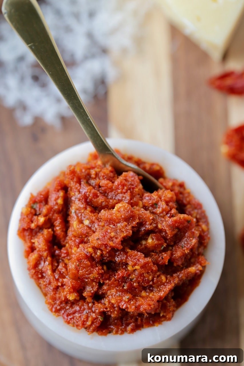 Sun Dried Tomato Pesto in white bowl with small gold spoon on wood cutting board