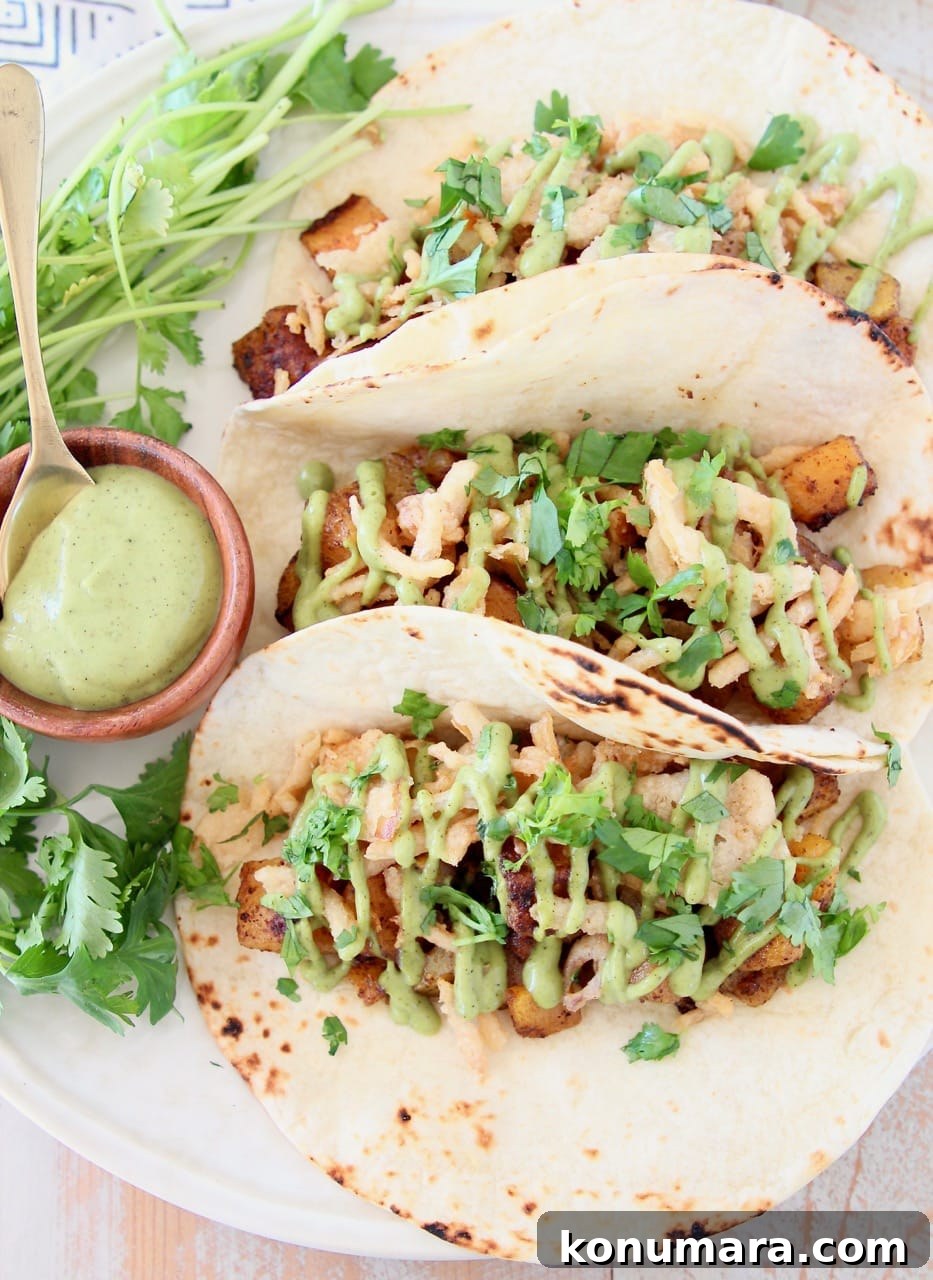Roasted Butternut Squash Tacos with Avocado and Lime 4 Butternut squash tacos in flour tortillas on plate with small bowl of creamy avocado sauce and fresh cilantro