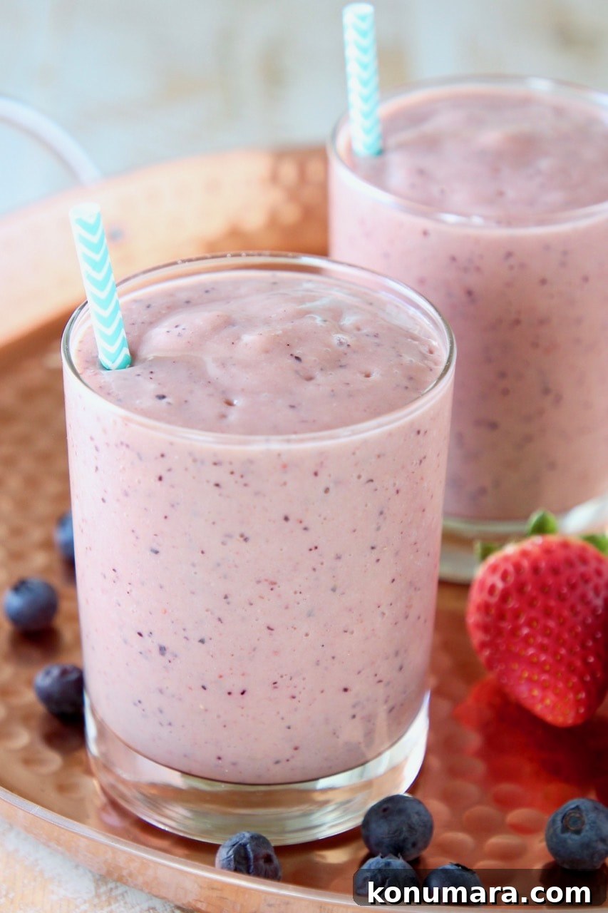 Fruit Smoothie for Heart Health 3 Fruit smoothie in glass with blue and white striped straw on copper tray with fresh blueberries and strawberries