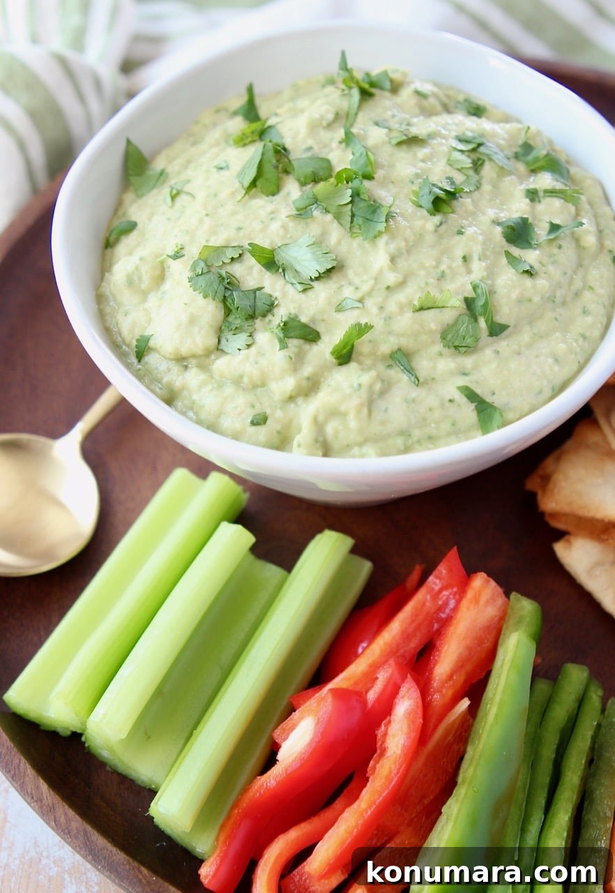 Spinach artichoke hummus in bowl with celery sticks, pita chips and bell peppers on the side