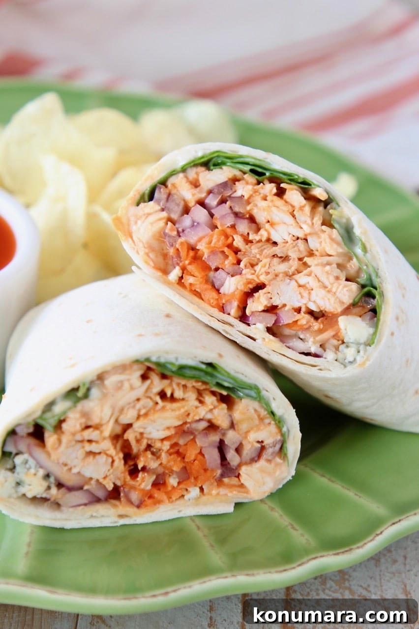 Buffalo chicken wrap cut in half and leaning on each other on green plate with potato chips