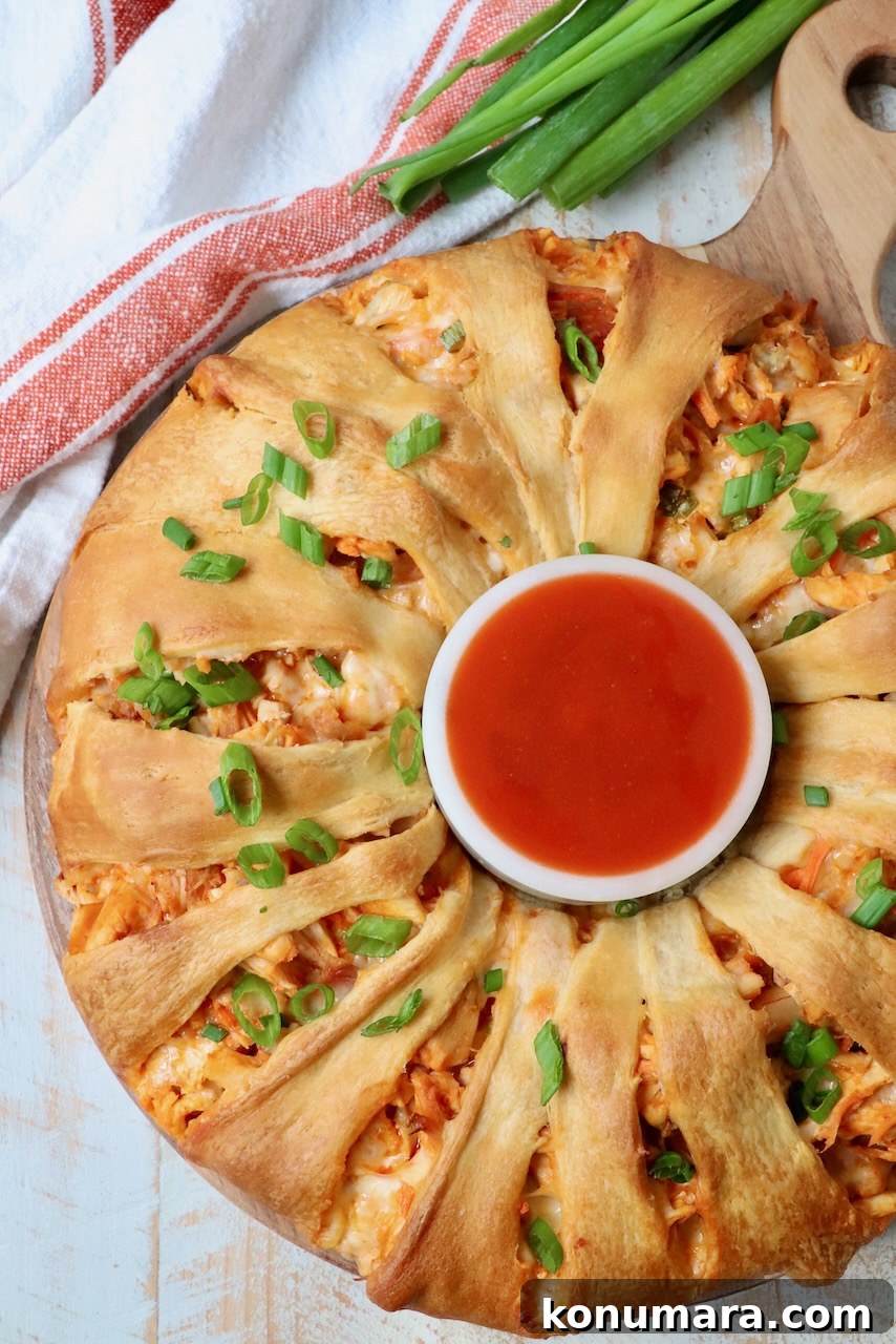 buffalo chicken crescent roll ring on a wood serving tray with a bowl of buffalo sauce in the middle