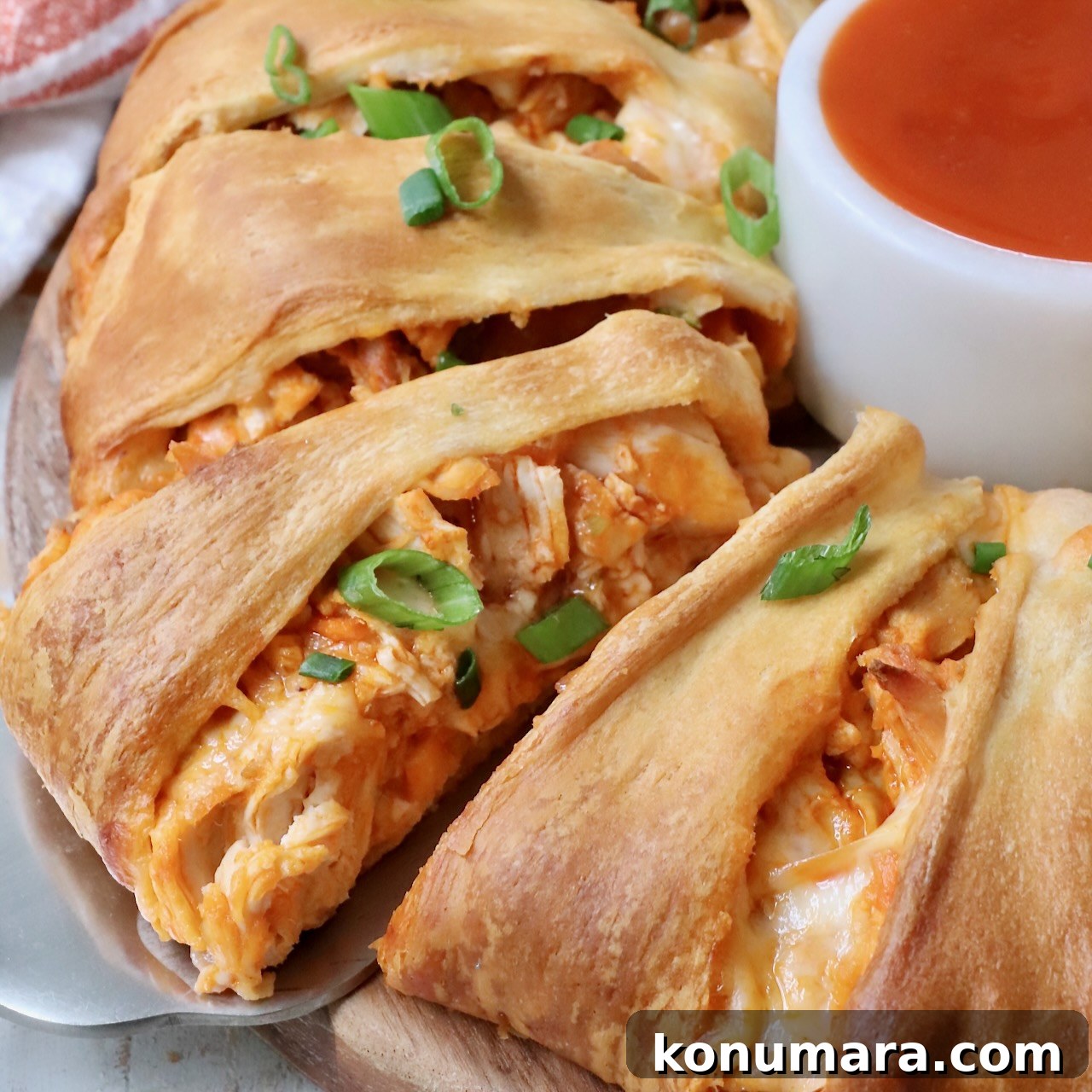 spatula under a piece of buffalo chicken taco ring with a small bowl of buffalo sauce on the side