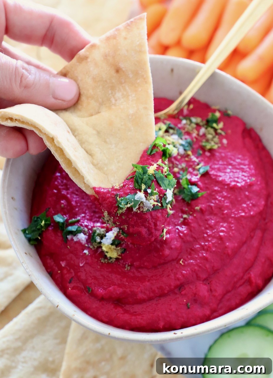 Creamy Roasted Beet Hummus with Lemon and Garlic 2 beet hummus in bowl with piece of pita bread dipped into the hummus