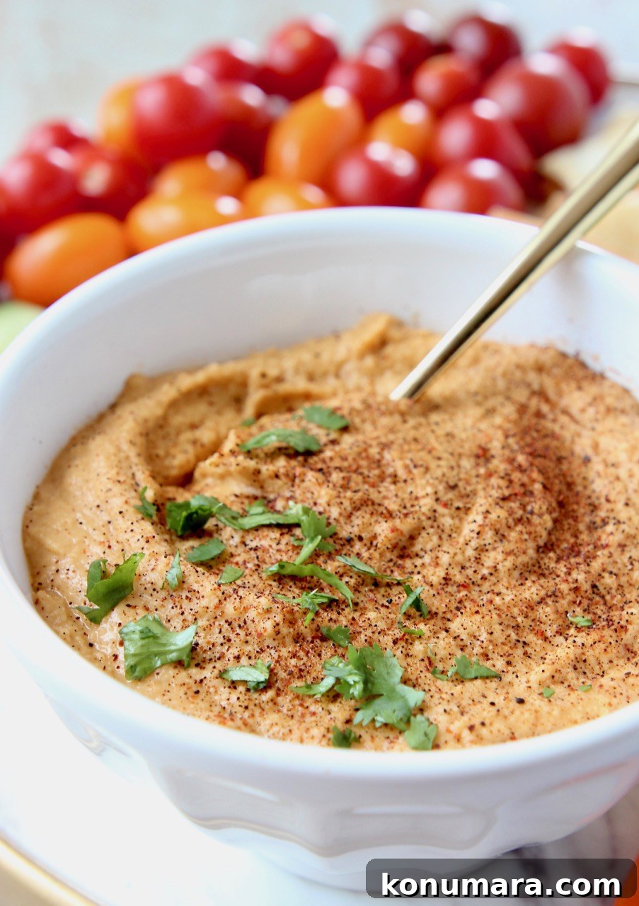 Sriracha hummus in white bowl with gold spoon