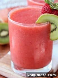 Strawberry slush in glass with kiwi slice and strawberry on the rim of the glass