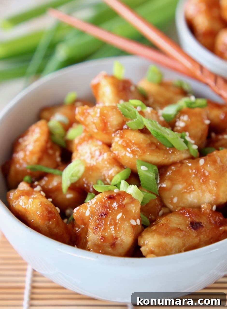 orange chicken in bowl with diced scallions and chopsticks