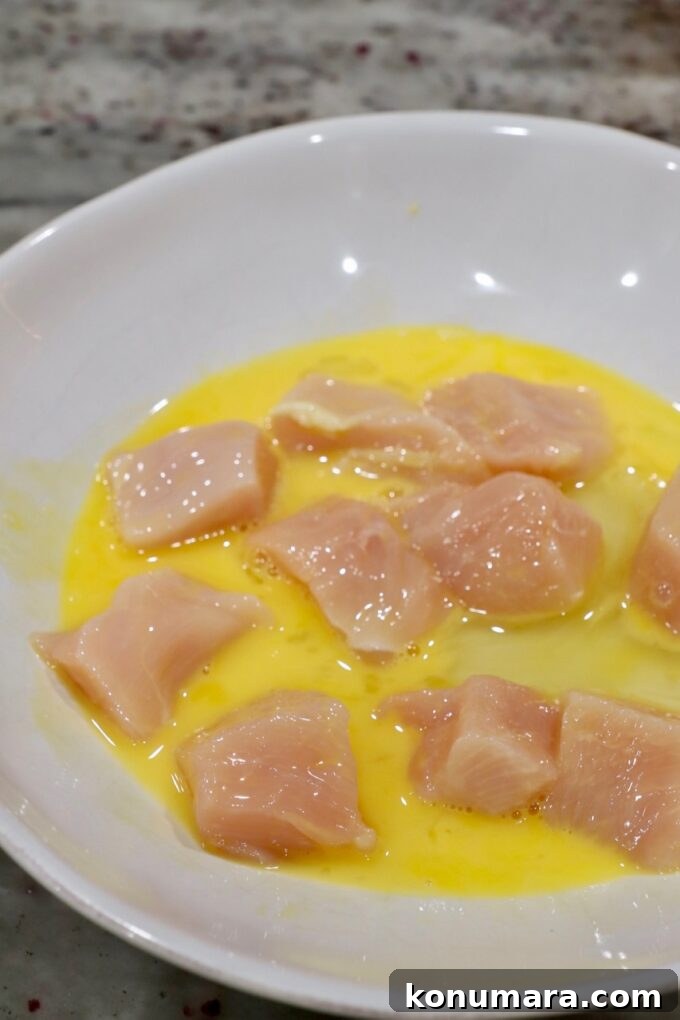 pieces of chicken dipped in a whisked egg in a bowl