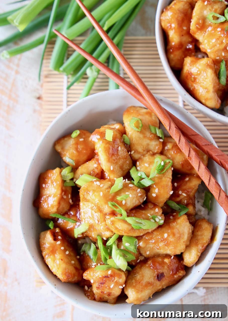 Orange chicken in bowl with diced scallions and wood chopsticks