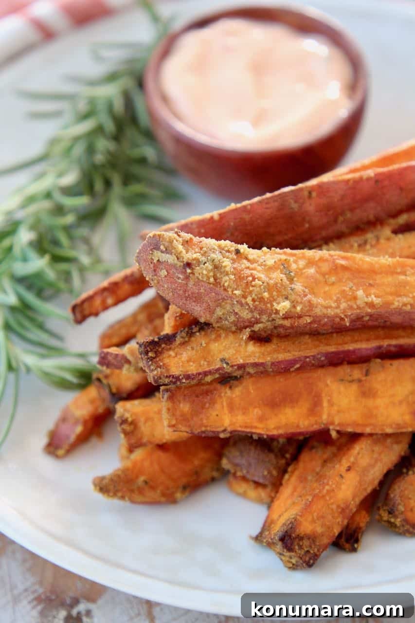 Sweet potato fries stacked up on plate with fresh rosemary sprig on the side