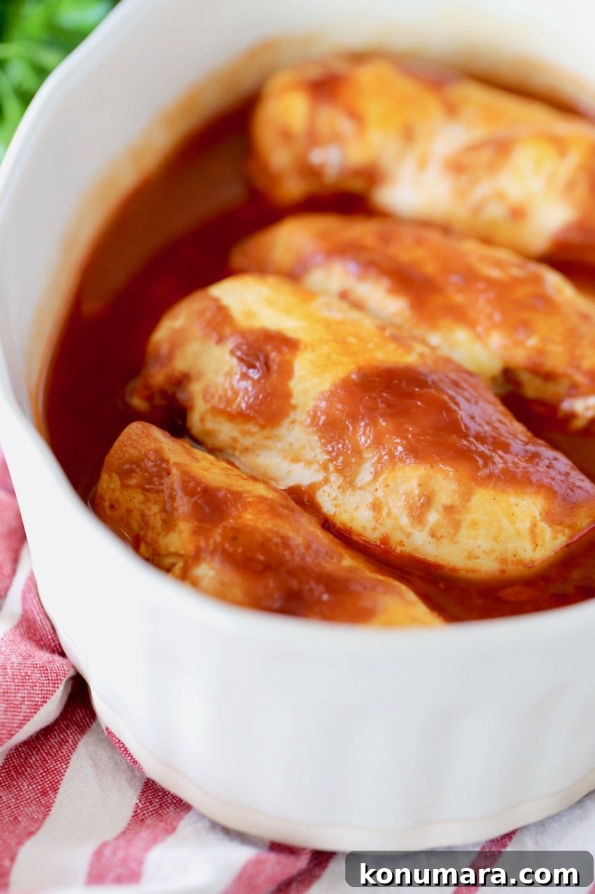 Oven Baked Buffalo BBQ Chicken 2 Baked chicken breasts in beige casserole dish, covered in buffalo bbq sauce, sitting on top of red and white striped towel