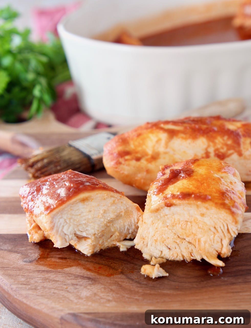 Oven Baked Buffalo BBQ Chicken 3 Two pieces of baked chicken on wood cutting board with one piece of chicken sliced in half and pastry brush in the background