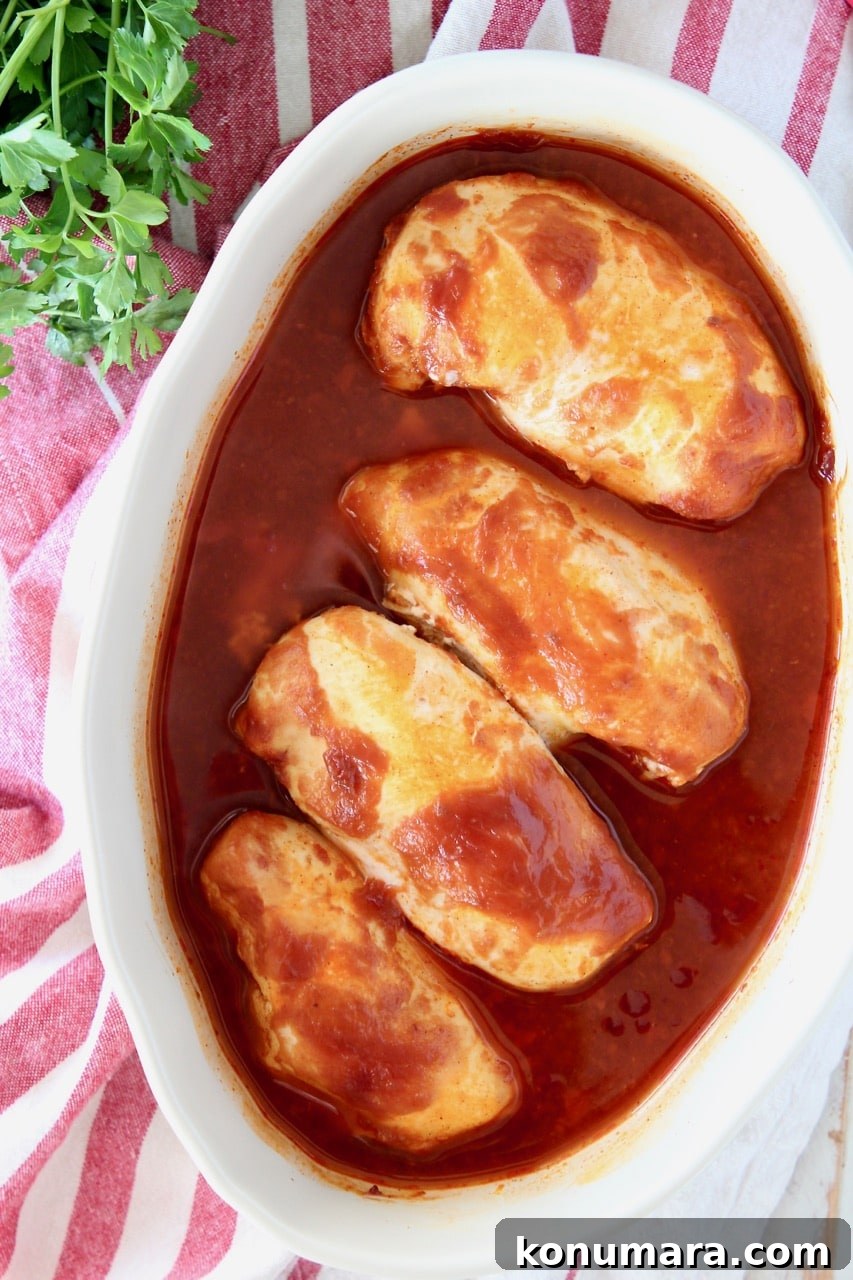 Oven Baked Buffalo BBQ Chicken 4 Overhead shot of baked chicken breasts in bbq sauce in oval baking dish, on top of red and white striped towel with fresh parsley on the side