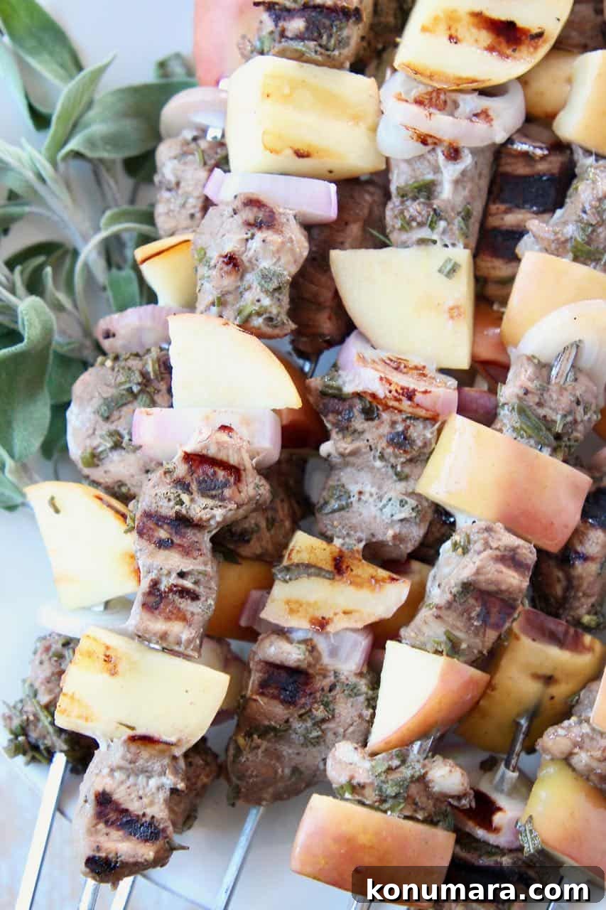 Pork tenderloin skewers with apples and shallots, stacked up on a plate with fresh herbs
