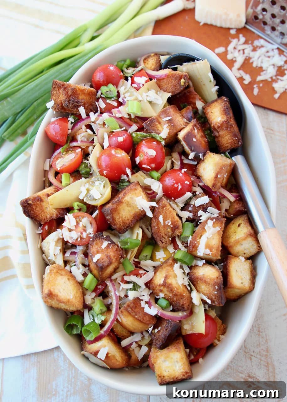 Tuscan Panzanella: Tomato, Cucumber & Bread Salad 2 Toasted bread cubes, cherry tomatoes and parmesan cheese in large oval bowl with spoon in bowl