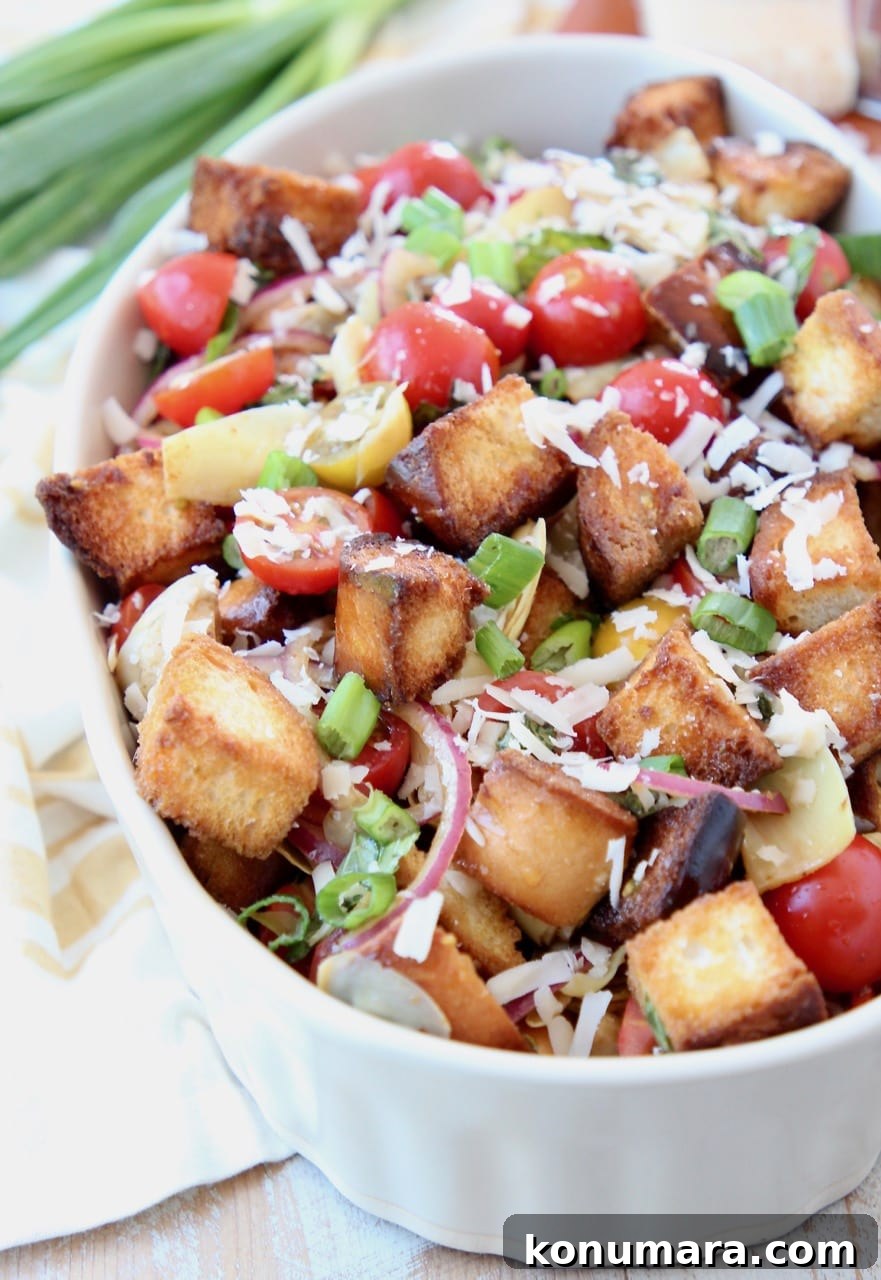 Tuscan Panzanella: Tomato, Cucumber & Bread Salad 5 Panzanella salad in bowl with toasted bread pieces and halved cherry tomatoes, topped with grated parmesan cheese
