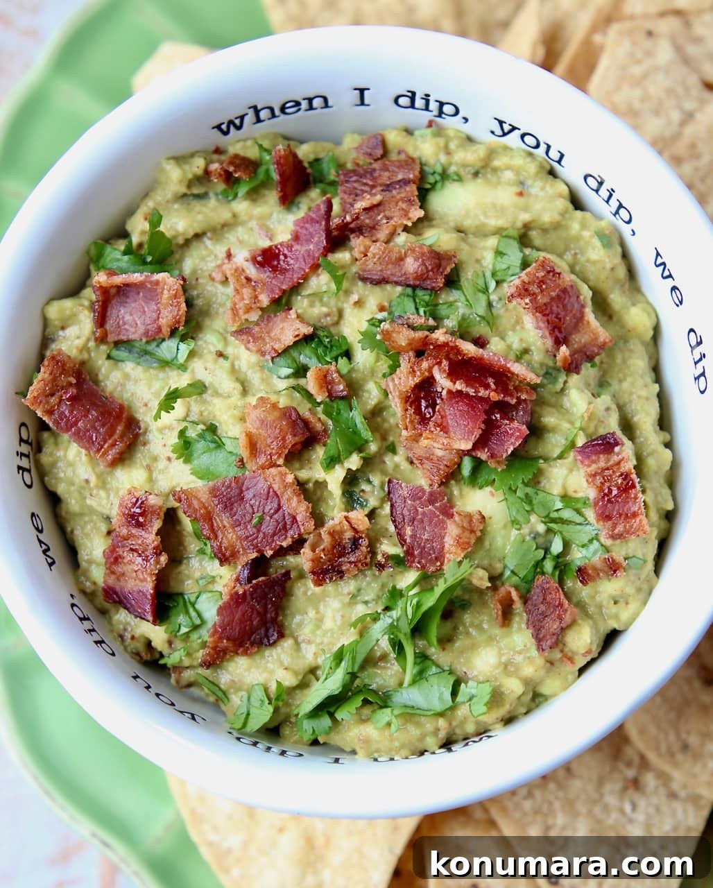 Guacamole in white bowl with crumbled cooked bacon on top