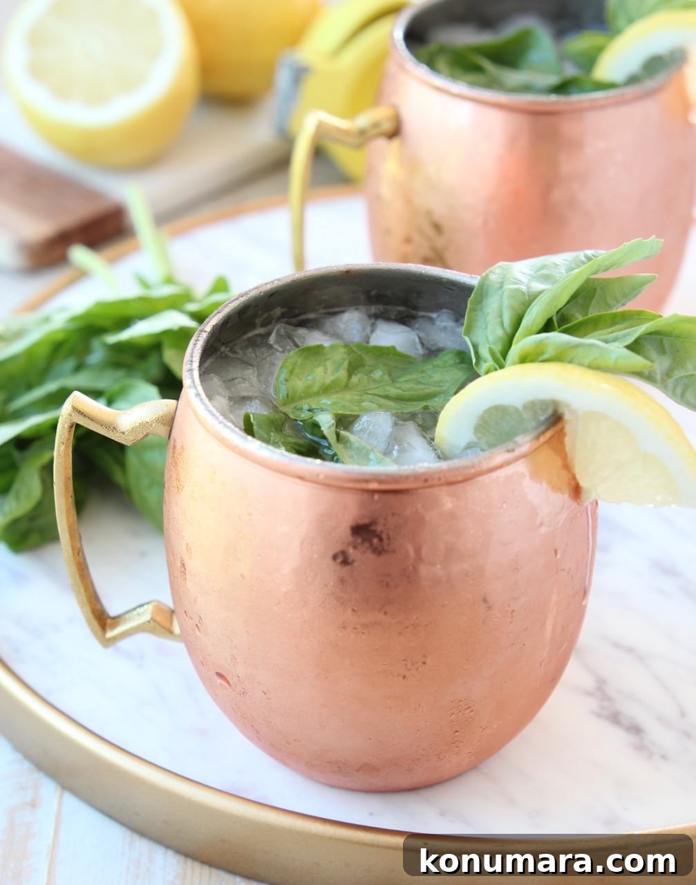 Peach and Basil Moscow Mule Cocktail Recipe 4 Copper mug filled with ice, vodka and ginger beer, on marble tray