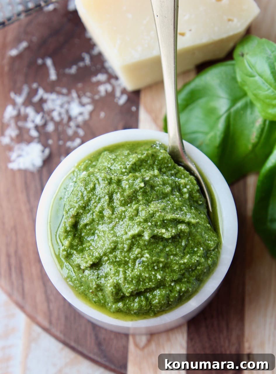 Overhead shot of basil pesto in a small white bowl with a small gold spoon in the bowl