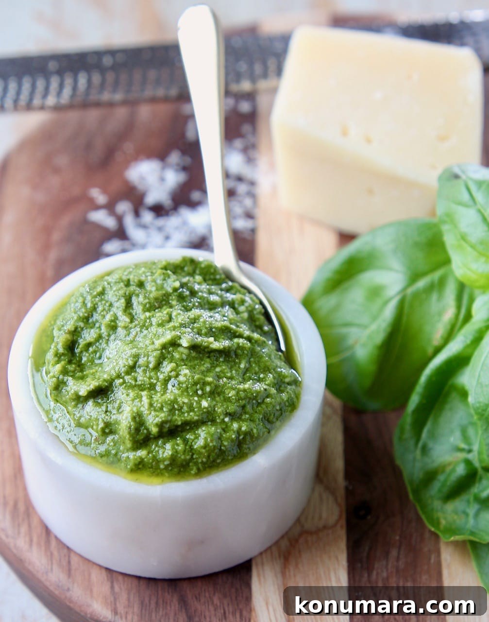 Basil pesto in small white bowl sitting next to fresh basil leaves and a block of parmesan cheese
