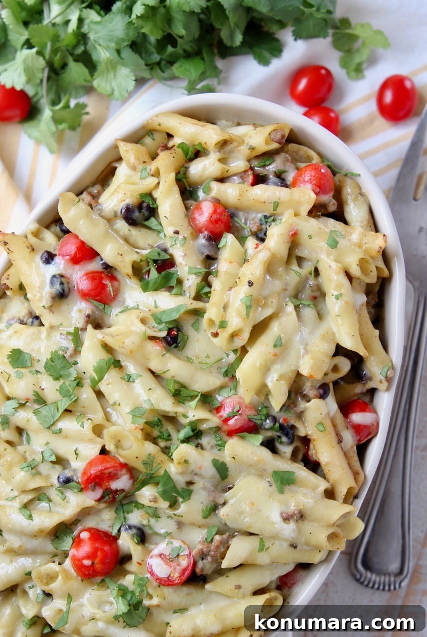 Baked taco pasta in a casserole dish with black beans, cherry tomatoes and cilantro