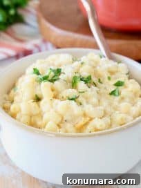 Butternut squash mac and cheese in white bowl with gold spoon on orange striped towel with fresh parsley