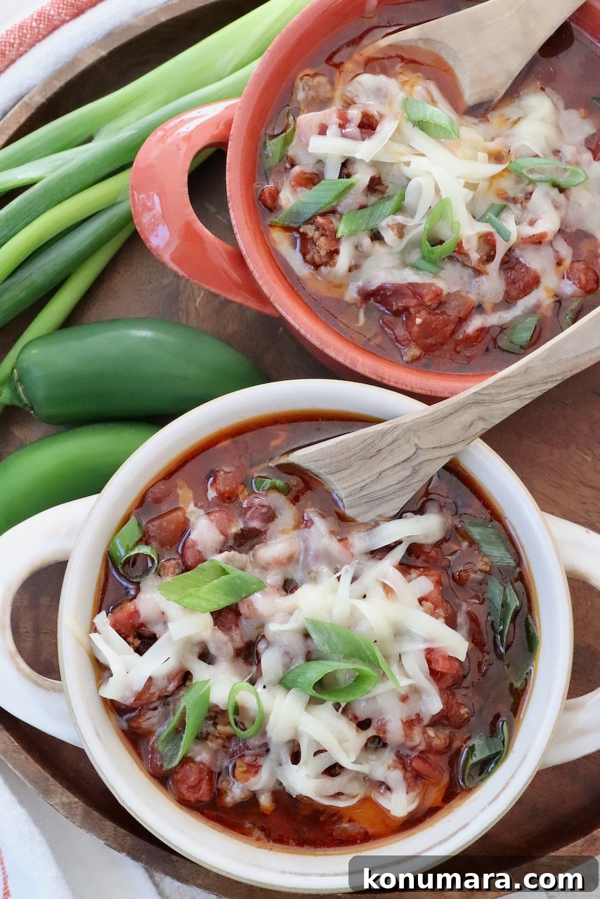 chili in bowls with spoons topped with shredded cheese and diced green onions
