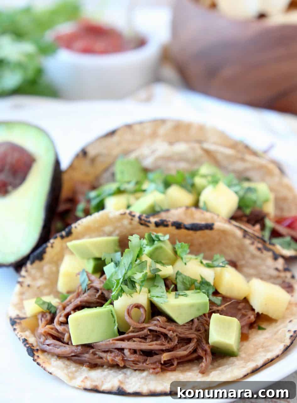 Shredded beef tacos topped with diced pineapple and avocado