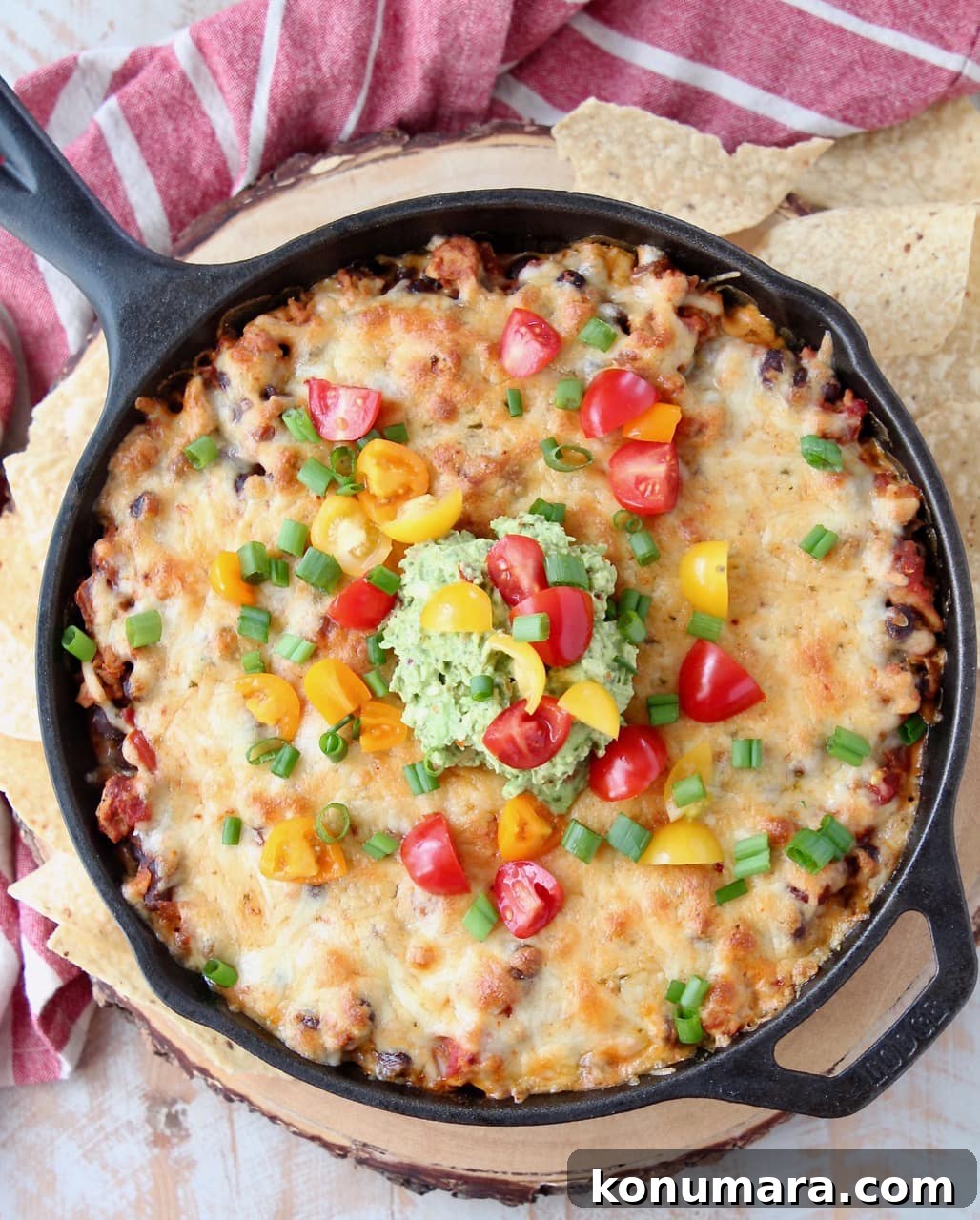 Overhead shot of cheesy taco dip baked in a cast iron skillet topped with diced cherry tomatoes and guacamole