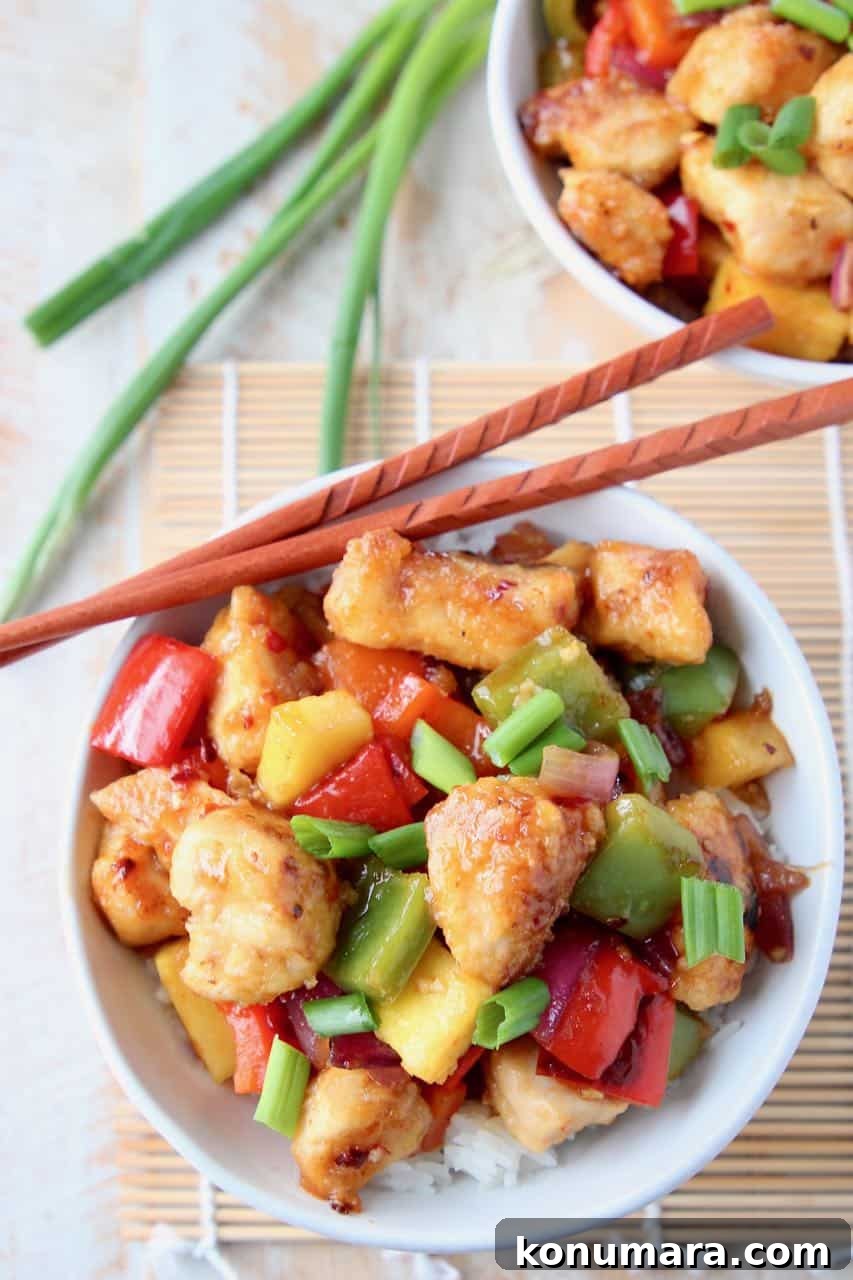 Sweet and sour chicken with pineapple and bell peppers on top of rice in bowl with chopsticks on the side