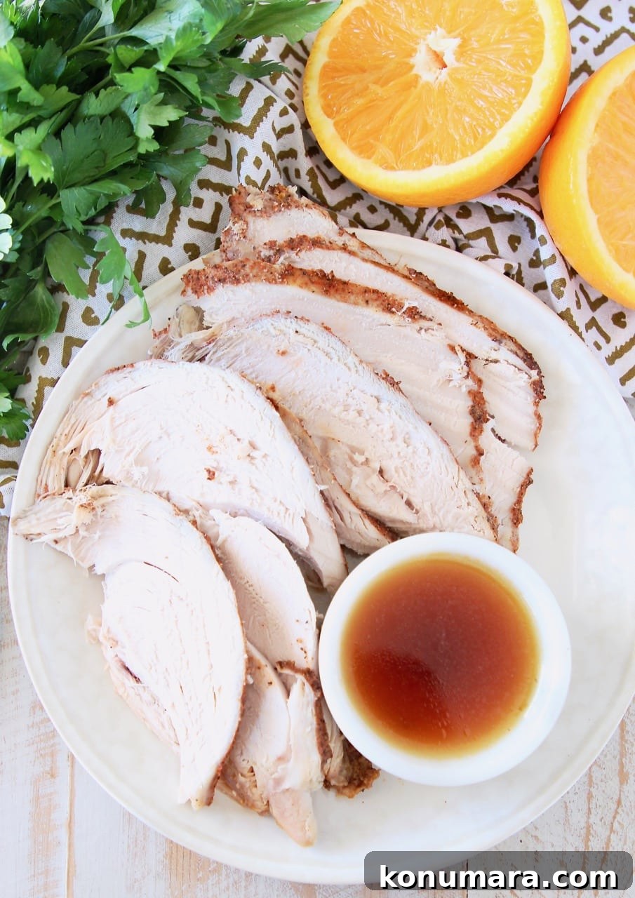 Slices of turkey breast on a white plate, with a side ramekin of orange bourbon glaze with sliced orange in background and fresh parsley bunch