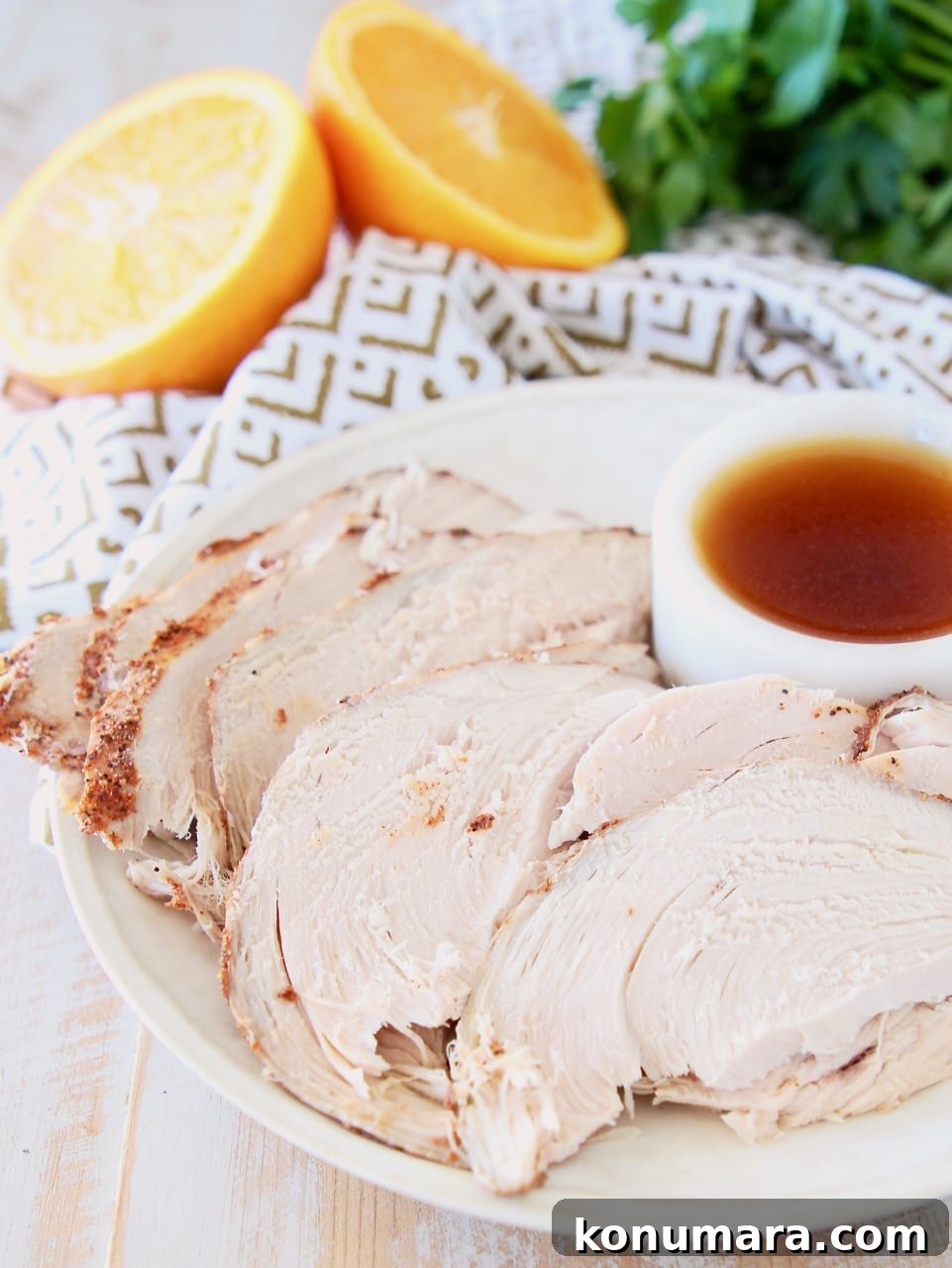 Slices of crock pot turkey breast on a plate with a white ramekin of orange bourbon glaze and a cut orange in the background with fresh parsley and a white patterned towel