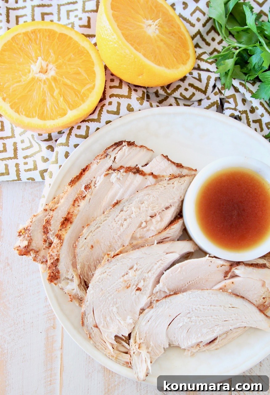 Slices of spice rubbed turkey breast on plate, next to small white bowl or orange bourbon sauce, with an orange cut in half next to the plate with fresh parsley