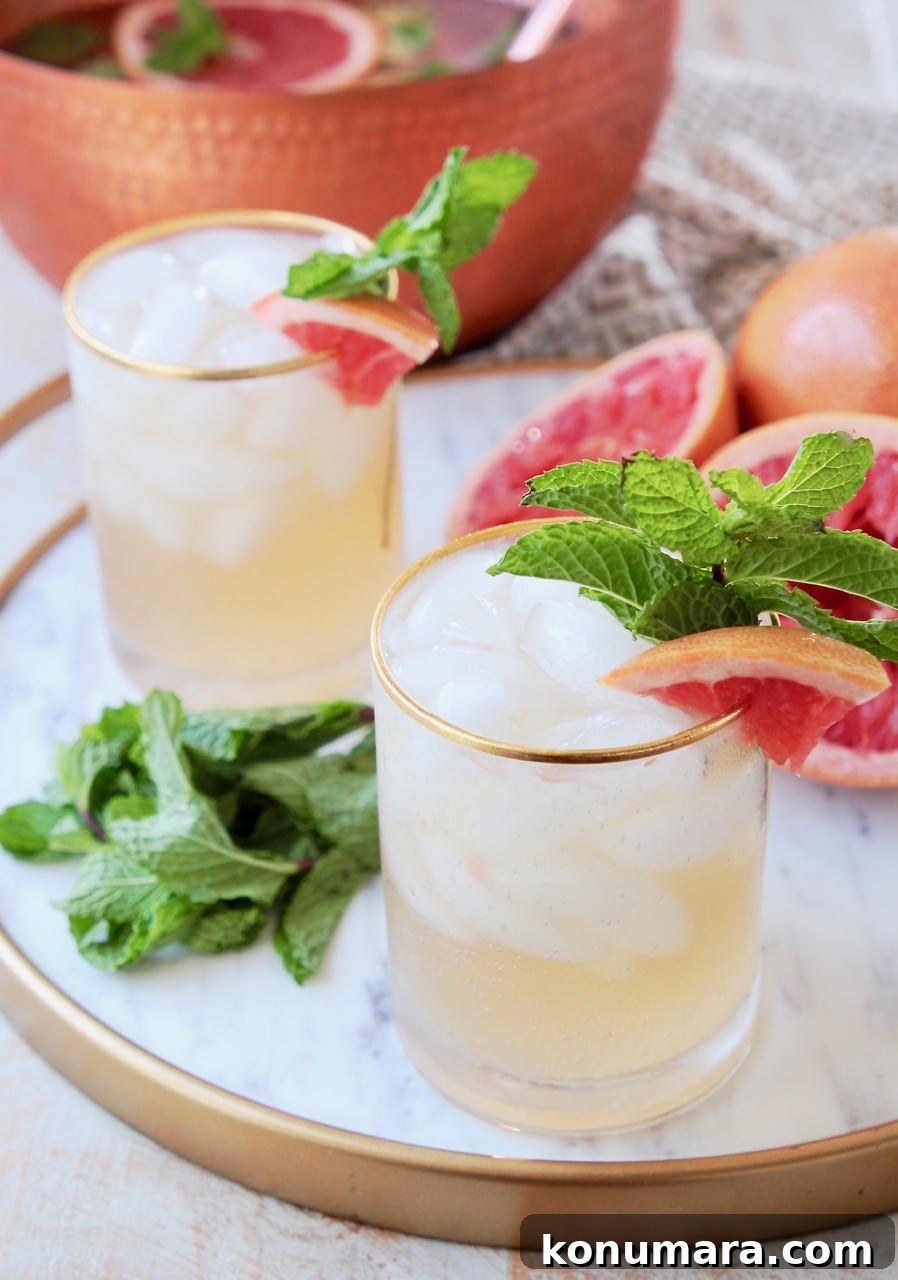 Grapefruit and Ginger Spiced Rum Punch Recipe 3 Glasses of spiced rum punch with gold rim, garnished with fresh mint and grapefruit slices, sitting on marble and gold serving tray with fresh mint leaves and squeezed grapefruit halves