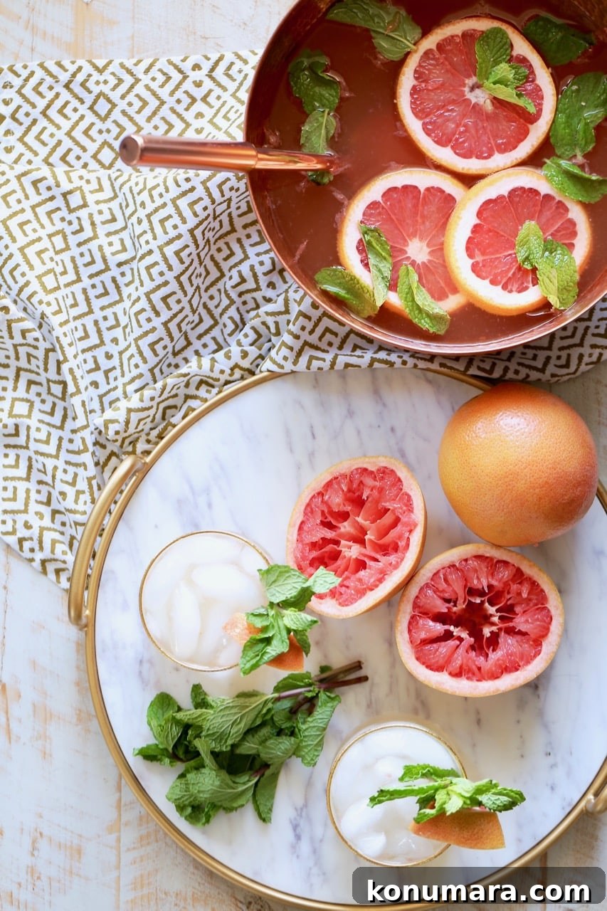 Grapefruit and Ginger Spiced Rum Punch Recipe 4 Rum punch in copper bowl with fresh grapefruit slices and mint springs, with a marble serving tray sitting next to it, topped with glasses of rum punch, grapefruits sliced open and fresh mint sprigs