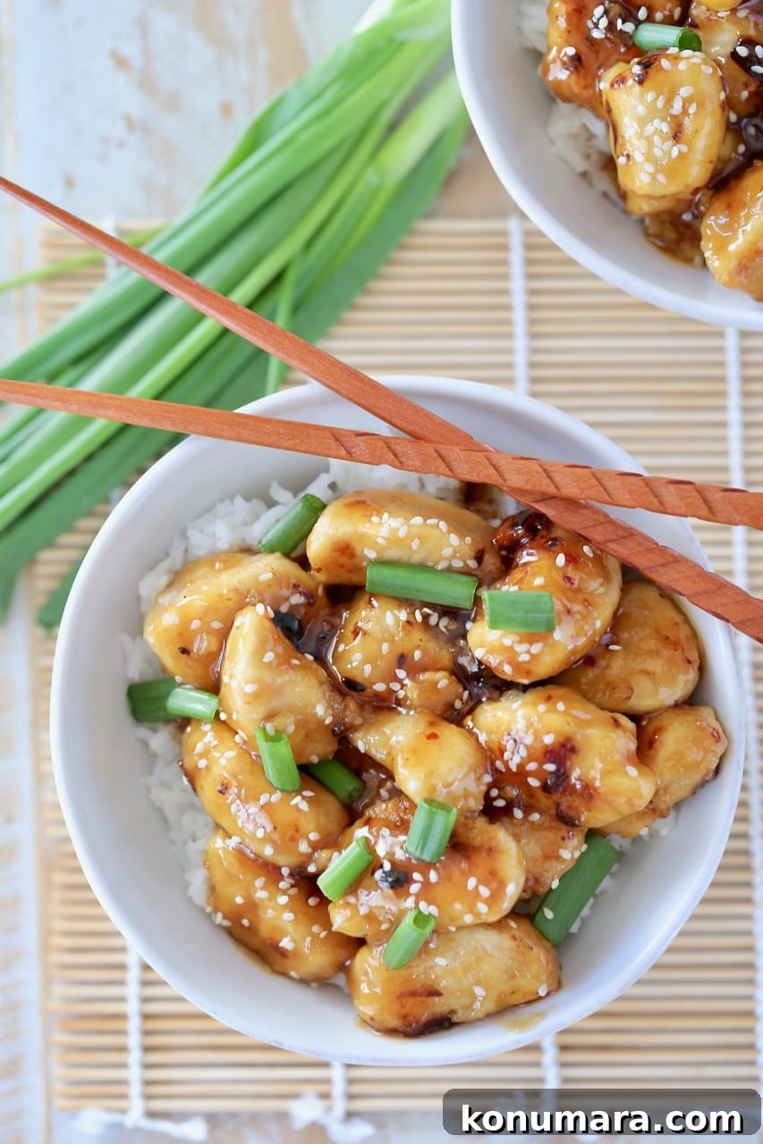 Gluten-Free Chinese Honey Chicken Recipe 5 Overhead shot of Chinese honey chicken in white bowl with white rice, green onions and sesame seeds with chopsticks on the side of the bowl and green onions next to the bowl