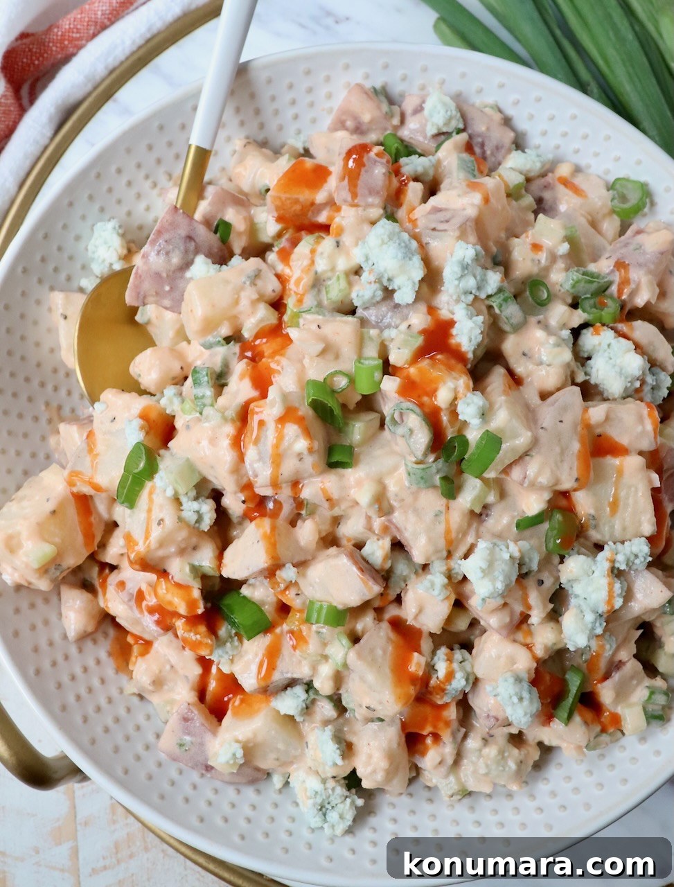 Buffalo Potato Salad with Blue Cheese and Celery 2 potato salad in bowl topped with a drizzle of buffalo sauce with a spoon in the bowl