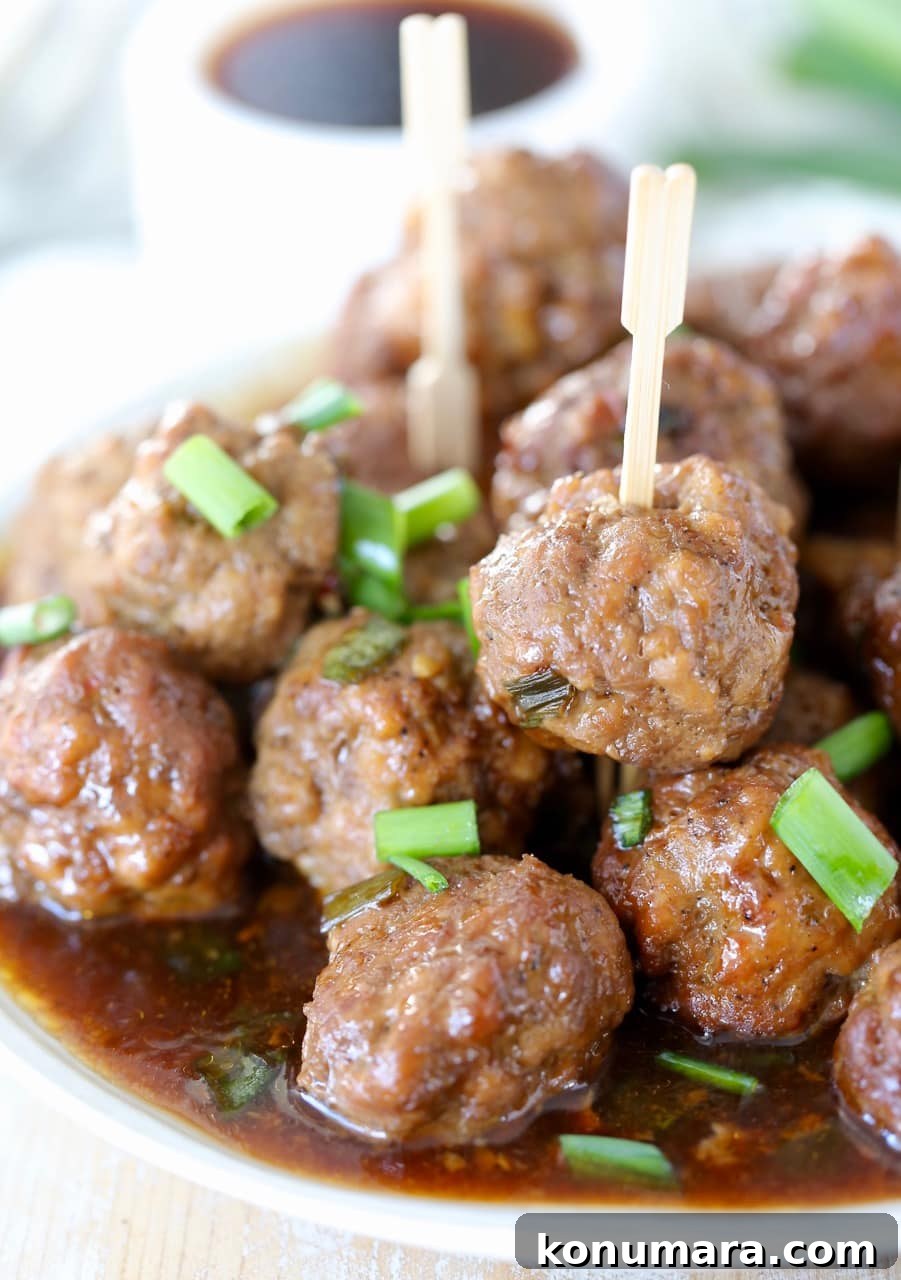 Slow Cooker Korean BBQ Meatballs with Gochujang Glaze 3 Korean BBQ meatballs piled on a plate topped with green onions with wooden skewers stuck in the meatballs