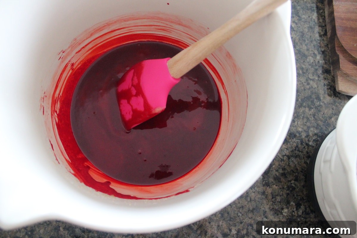 Butter, sugar, vanilla, eggs, and red food coloring mixed in a white bowl. 