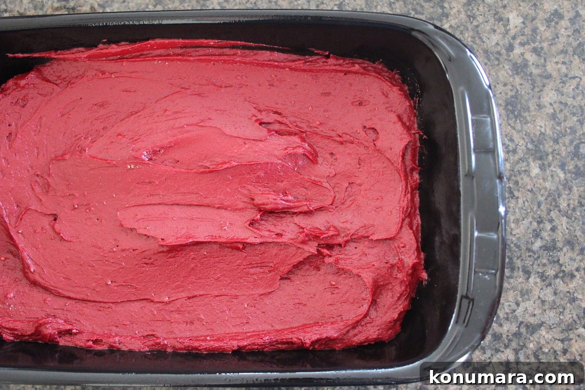 Red velvet brownie batter spread in the bottom of a baking dish.