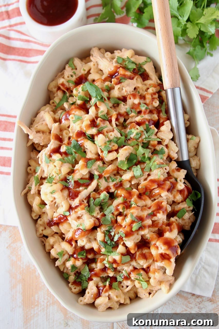 Smoky BBQ Chicken Mac and Cheese Recipe 4 Mac and cheese in large oval baking dish, topped with bbq sauce, with a large serving spoon in the dish