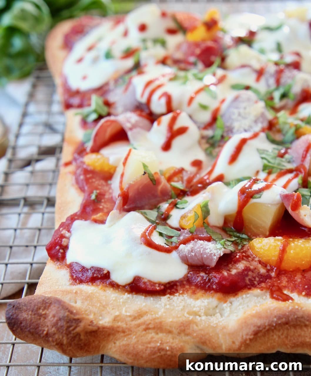 Hawaiian pizza topped with sriracha, cheese and pineapple on a wire rack