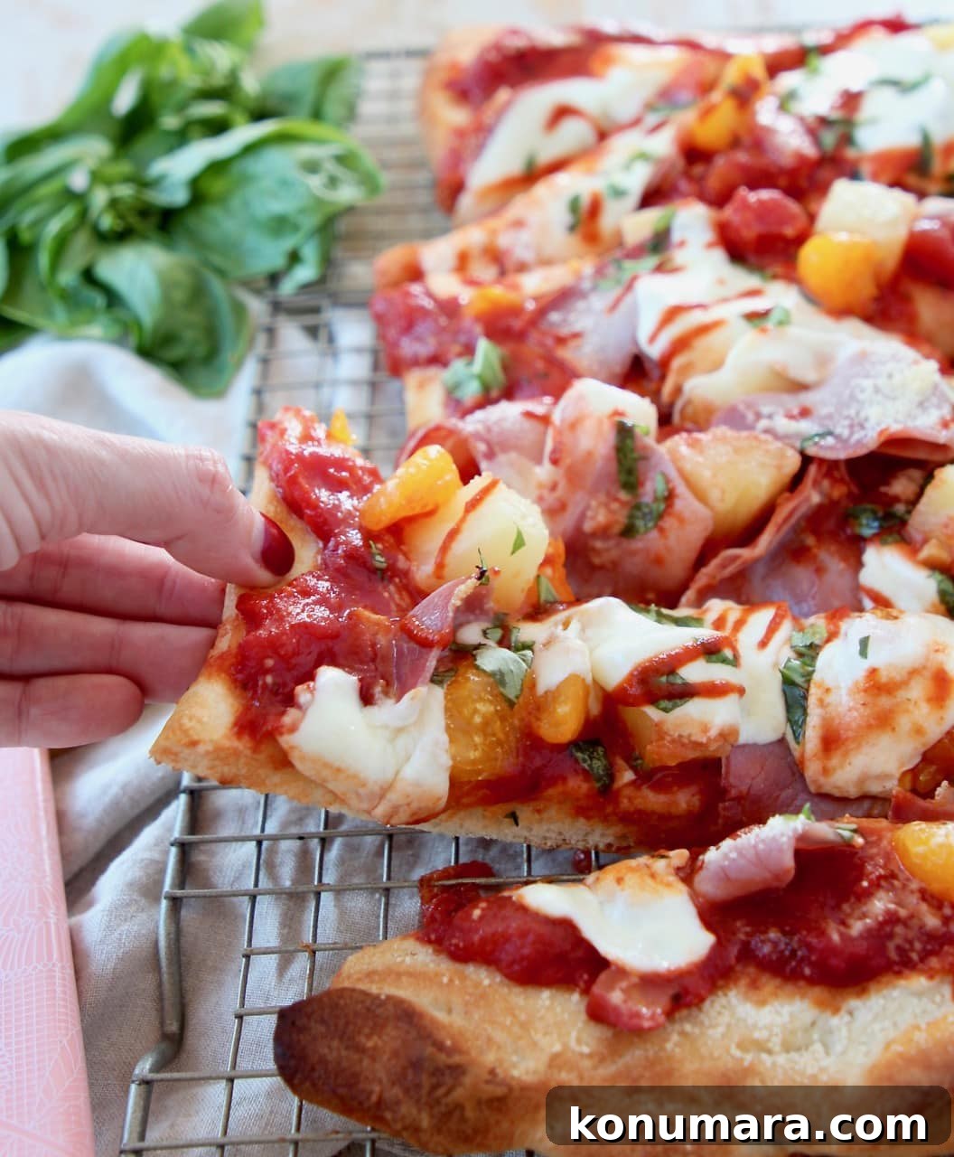 Hand grabbing a slice of Hawaiian pizza off of a wire baking rack